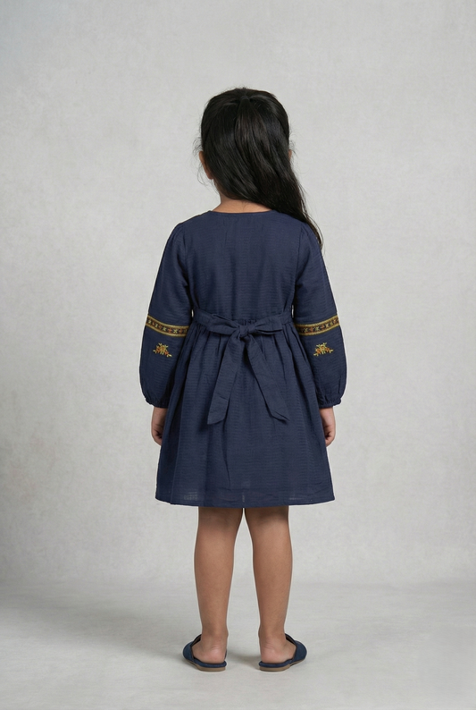 Girl wearing navy blue embroidered cotton frock with long sleeves, viewed from back
