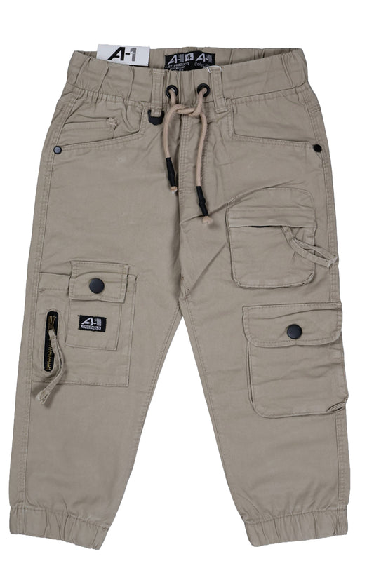 A single piece of children's utility cargo joggers in a light khaki or stone color. The design features a multi-pocket layout including large side flap pockets with black buttons and a vertical zipper detail on the right leg. It has a comfortable elastic waistband with a striped drawstring and elasticated ankle cuffs, shown as a flat lay against a neutral background.