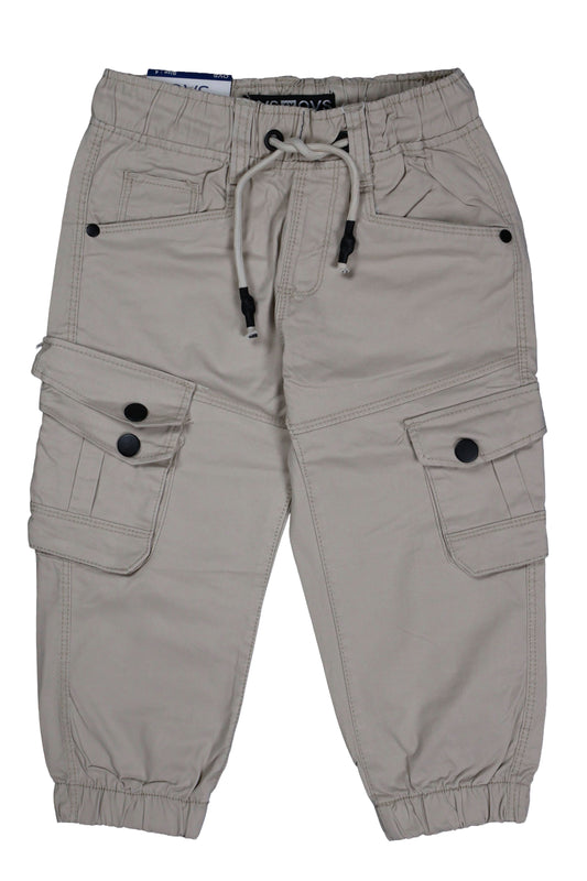 A single piece of children's utility cargo joggers in a light beige or stone color. The design features a comfortable elastic waistband with a matching drawstring, elasticated ankle cuffs, and two large side cargo pockets with secure black button closures. The garment is shown as a flat lay against a neutral background.