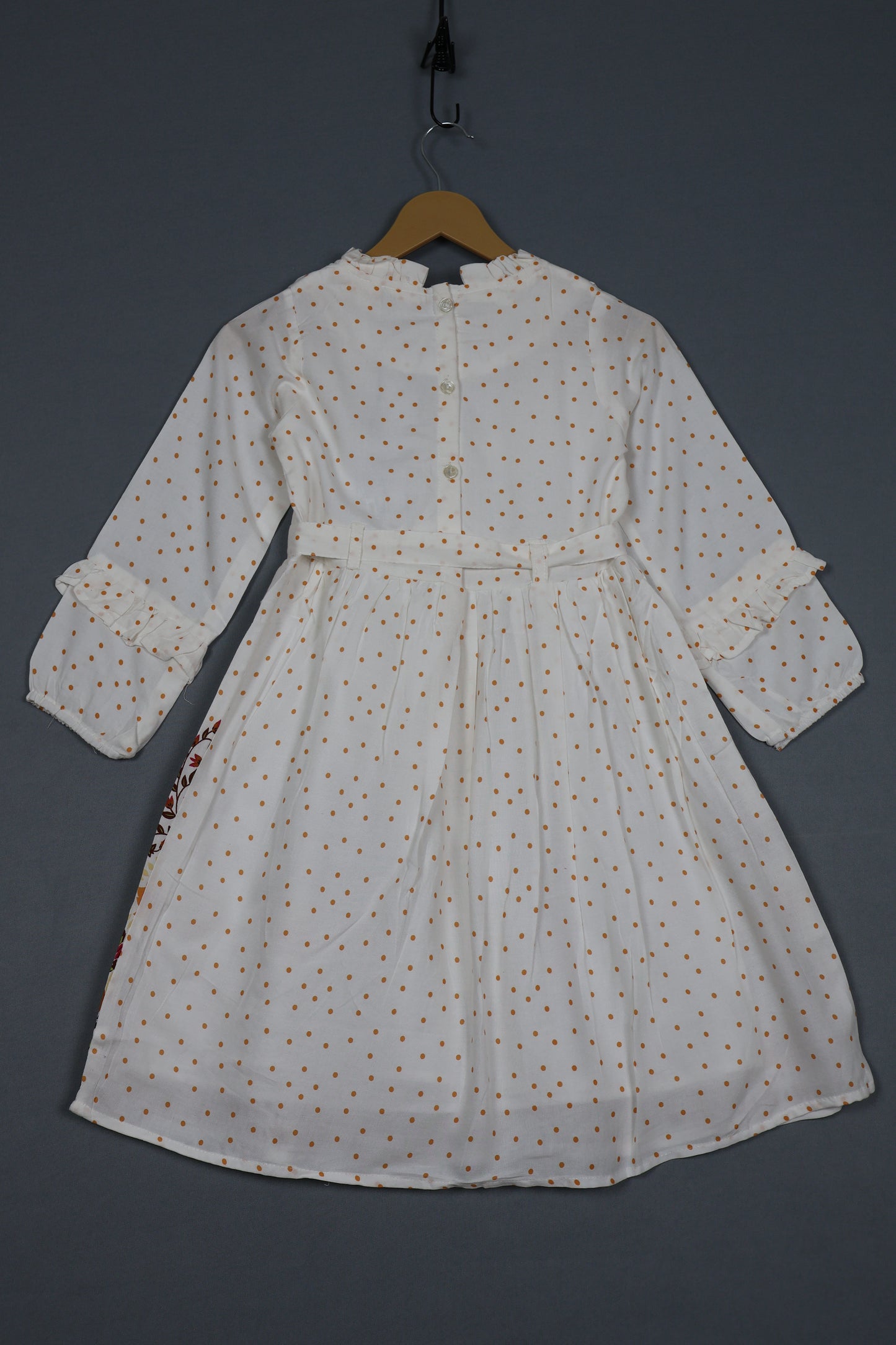White cotton kids dress with brown polka dots, long sleeves, and ruffle details