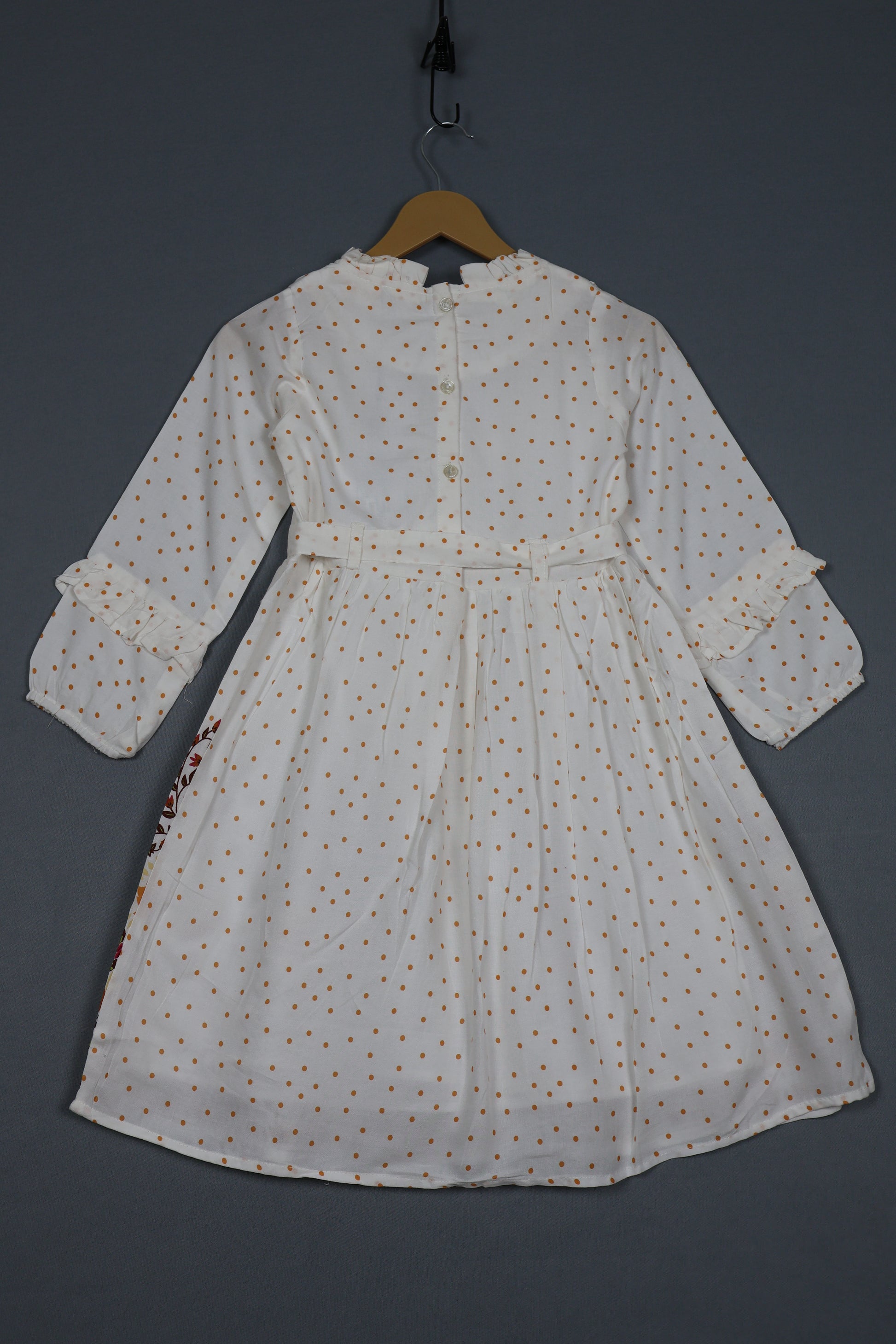 White cotton kids dress with brown polka dots, long sleeves, and ruffle details