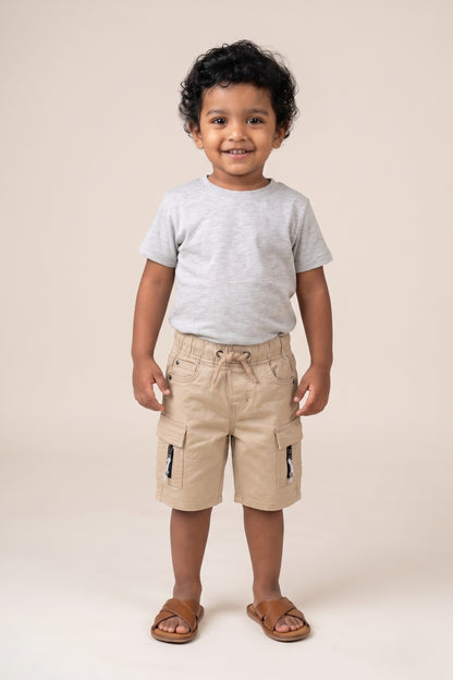 A kid wearing FYST brand lightweight khaki cargo shorts featuring an elasticated drawstring waistband, side flap pockets with decorative zipper details, and a comfortable knee-length fit.