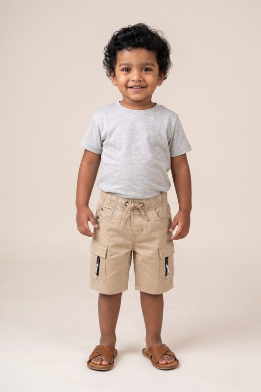 A kid wearing FYST brand lightweight khaki cargo shorts featuring an elasticated drawstring waistband, side flap pockets with decorative zipper details, and a comfortable knee-length fit.