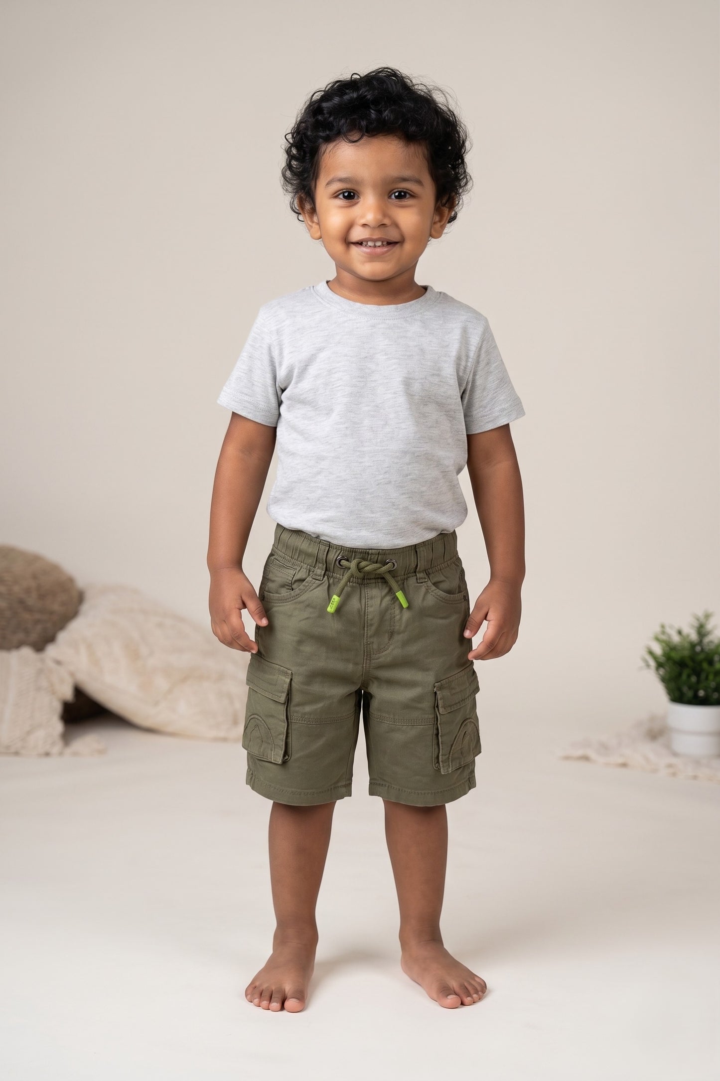 A kid wearing FYST brand lightweight olive green cargo shorts featuring a comfortable elastic drawstring waistband with lime green tips and multiple functional side flap pockets.