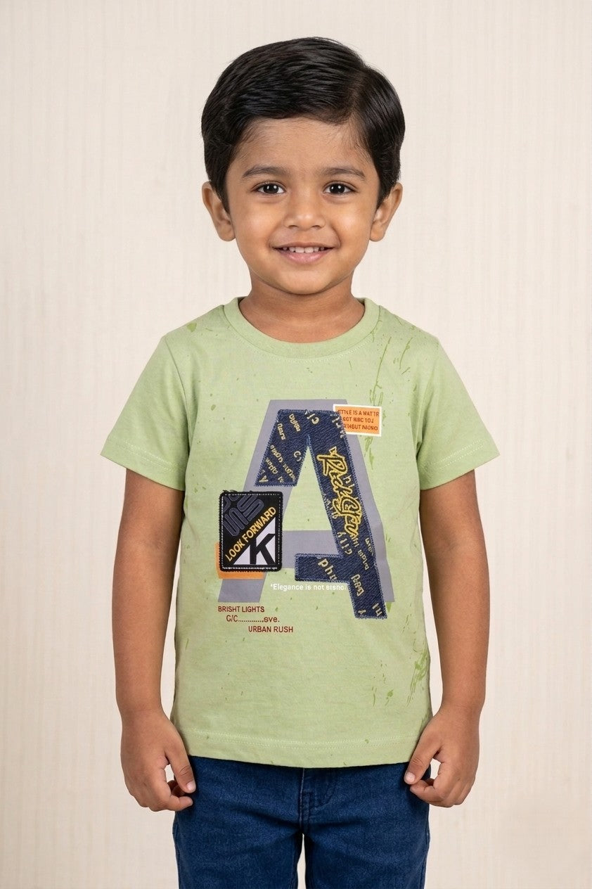 A kid wearing a FYST brand sage green short-sleeved t-shirt featuring a large "A" graphic with denim-style textures and "LOOK FORWARD" text, paired with dark blue denim bottoms.