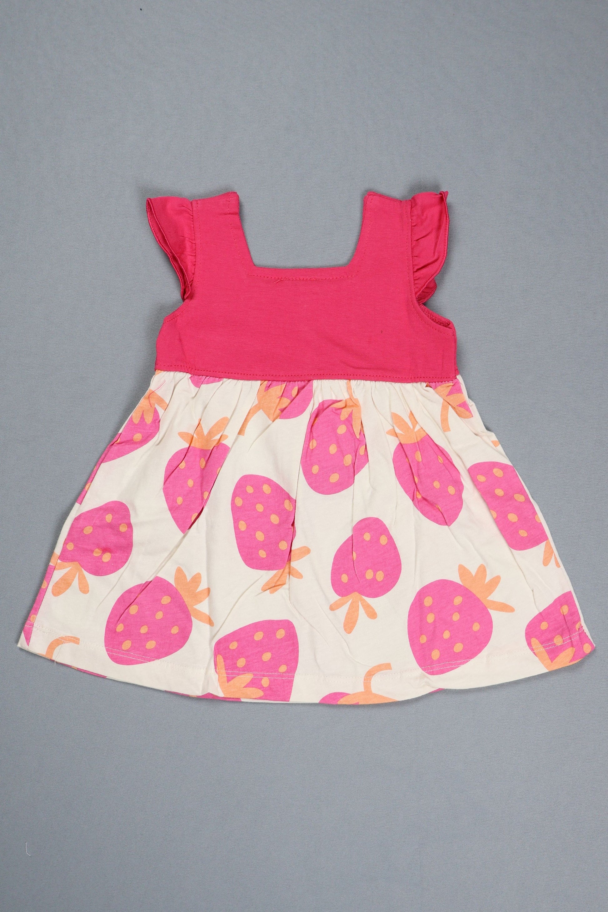 Children's dress with pink top and strawberry patterned skirt on a gray background