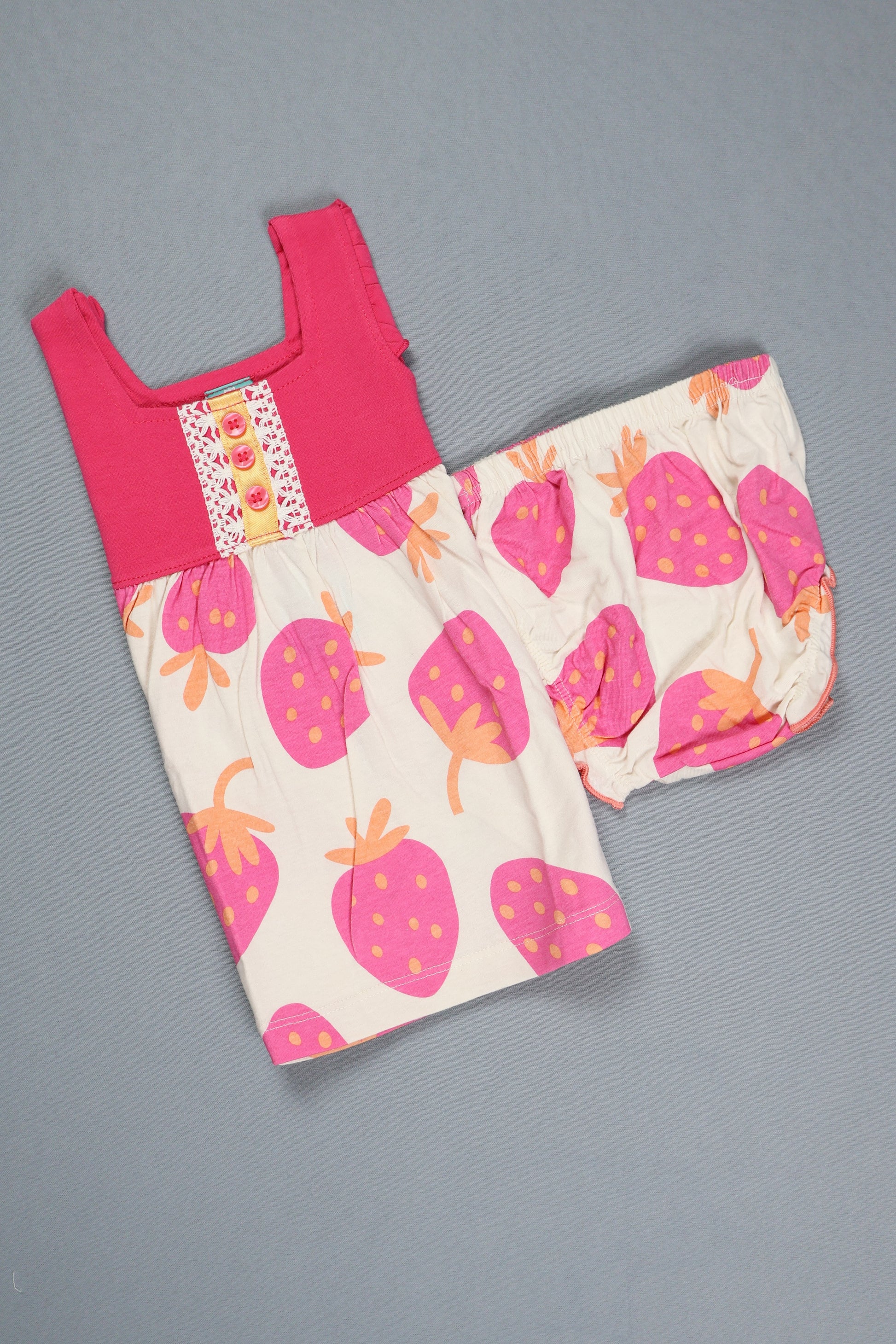 Children's outfit with pink top and strawberry patterned pants on a gray background