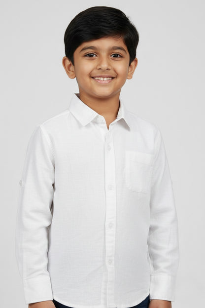A smiling young boy wearing a Fyst brand solid white long-sleeve cotton shirt. The shirt features a classic spread collar, matching white buttons, a single chest pocket, and a clean, textured fabric finish. He is posed against a light grey background, showcasing the shirt's bright, formal look and high-quality tailoring.