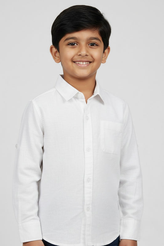 A smiling young boy wearing a Fyst brand solid white long-sleeve cotton shirt. The shirt features a classic spread collar, matching white buttons, a single chest pocket, and a clean, textured fabric finish. He is posed against a light grey background, showcasing the shirt's bright, formal look and high-quality tailoring.