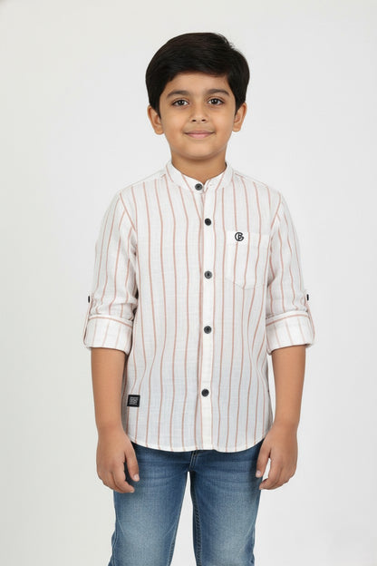 A young boy models a Fyst brand long-sleeve, linen-texture button-down shirt with a mandarin collar. The shirt is off-white with thin vertical brown pinstripes and features contrasting black buttons and rolled-up sleeves, paired with blue jeans.