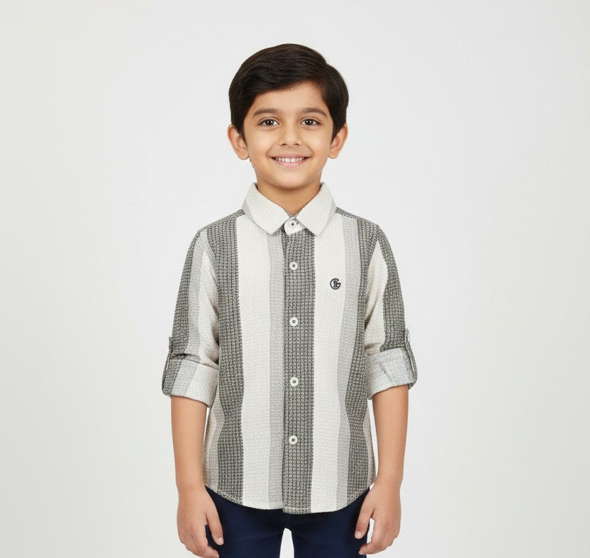A young boy smiling in a professional studio setting, modeling a Fyst brand button-down shirt featuring wide vertical stripes in white, light grey, and a textured charcoal grey