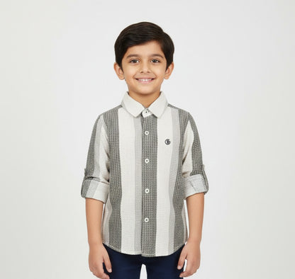 A young boy smiling in a professional studio setting, modeling a Fyst brand button-down shirt featuring wide vertical stripes in white, light grey, and a textured charcoal grey