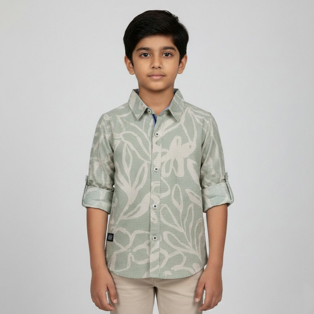 A young boy showcasing a Fyst sage green button-down shirt with a large cream abstract floral print and roll-up sleeve tabs