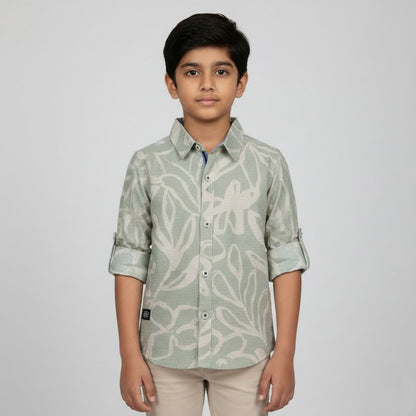 A young boy showcasing a Fyst sage green button-down shirt with a large cream abstract floral print and roll-up sleeve tabs