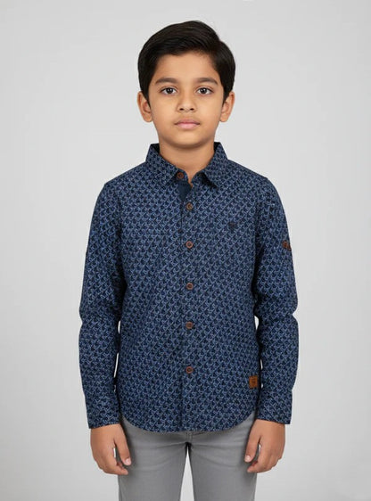 A young boy modeling a Fyst brand dark navy blue button-down shirt featuring a dense, repeating geometric diamond pattern. The shirt has contrasting brown buttons, a structured collar, and long sleeves, presented in a professional studio shot against a light grey background.
