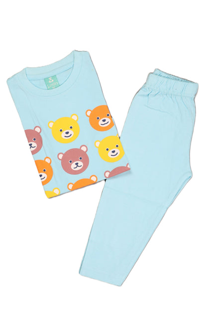 A flat lay of a light blue children's long-sleeve pajama set. The folded top features a repeating grid pattern of multicolored bear faces in yellow, orange, and brown, paired with matching solid light blue full-length pajama pants.