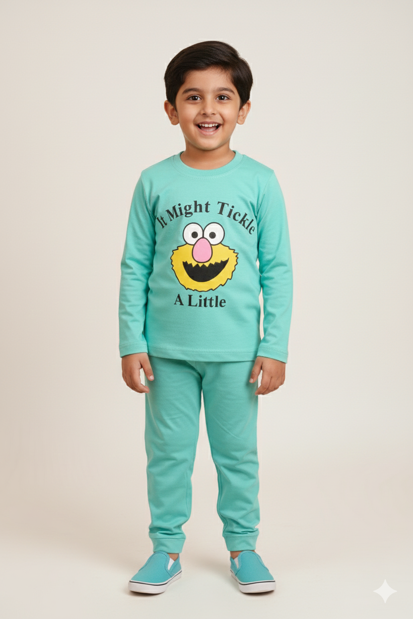 A young boy modeling a matching aqua blue long-sleeve pajama set. The top features a whimsical yellow character face with the playful text "It Might Tickle A Little." He is standing against a neutral background wearing matching aqua blue slip-on shoes.