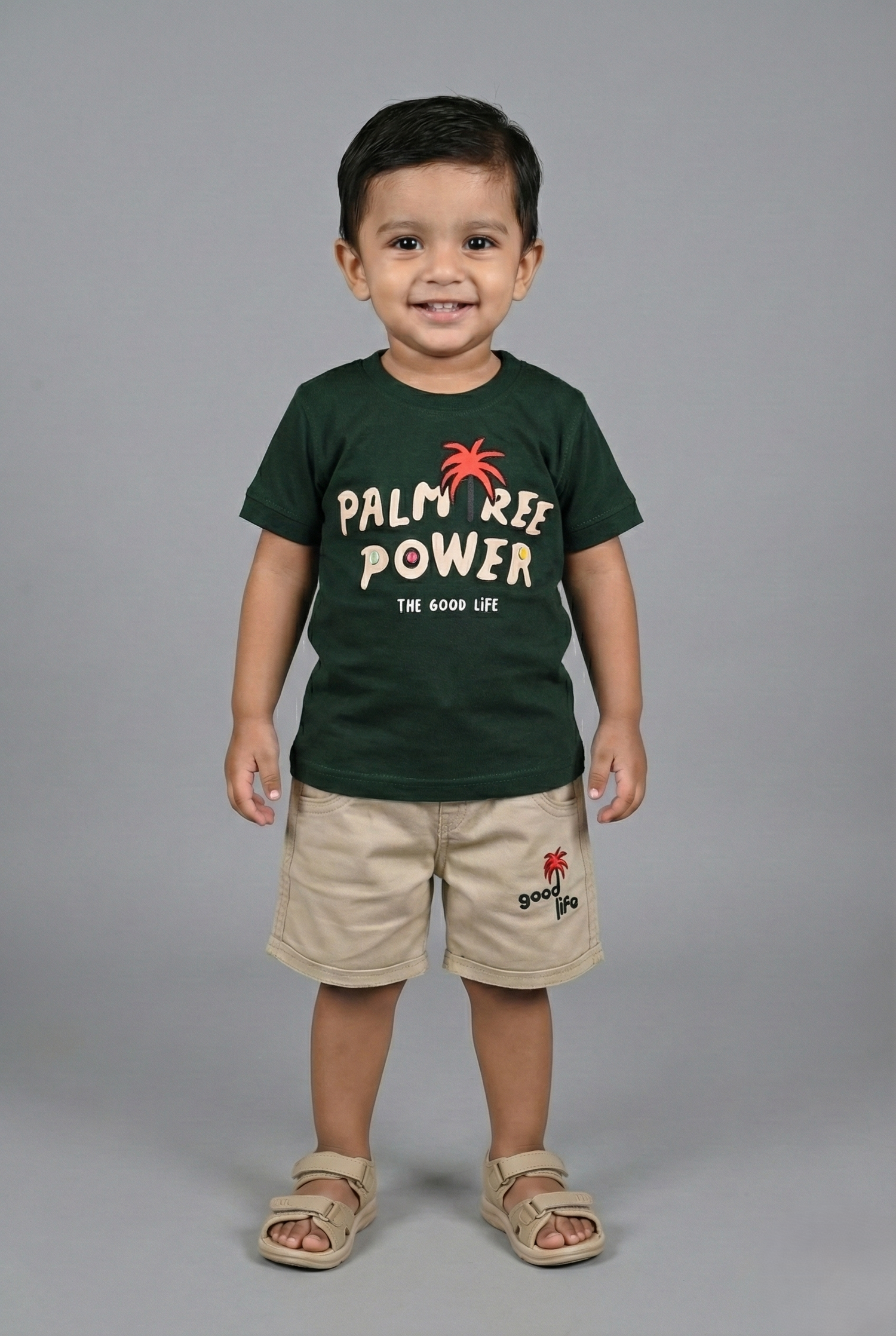 Child wearing a green 'Palm Tree Power' t-shirt and beige shorts on a gray background