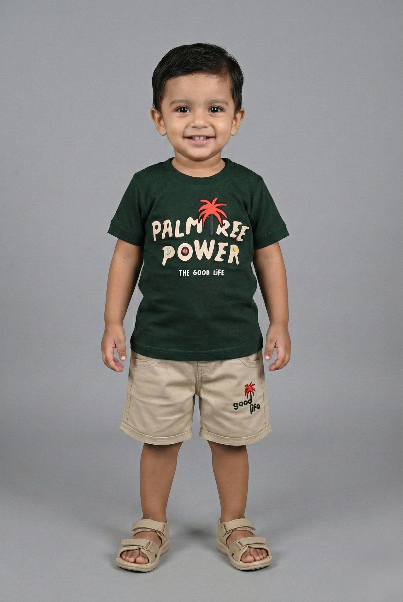Child wearing a green 'Palm Tree Power' t-shirt and beige shorts on a gray background