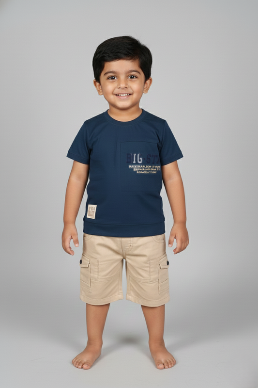 A young boy modeling a classic navy blue and beige summer set. The navy short-sleeve t-shirt features a small decorative chest pocket with light-colored typography. It is paired with matching beige cargo-style shorts. He is posing against a neutral grey studio background.
