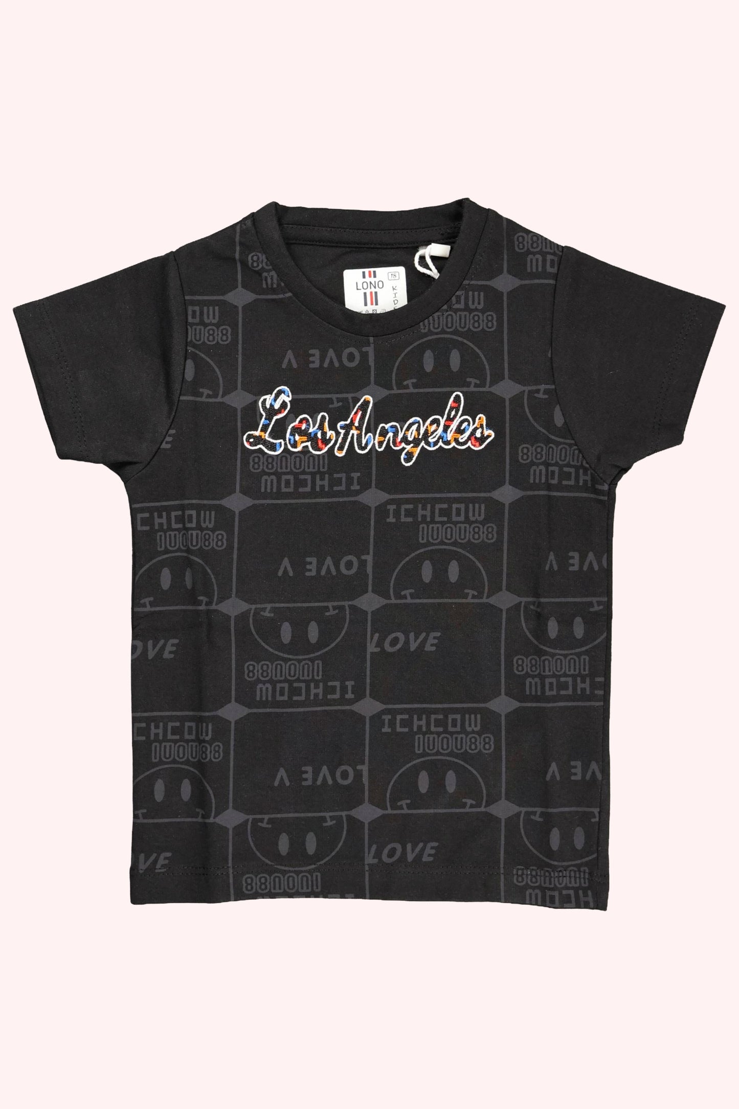 A children's black short-sleeve t-shirt. The front features "Los Angeles" written in a colorful script font over a subtle, all-over dark grey repeating "Love" typography pattern. The shirt is displayed as a flat lay against a light pink and white background.