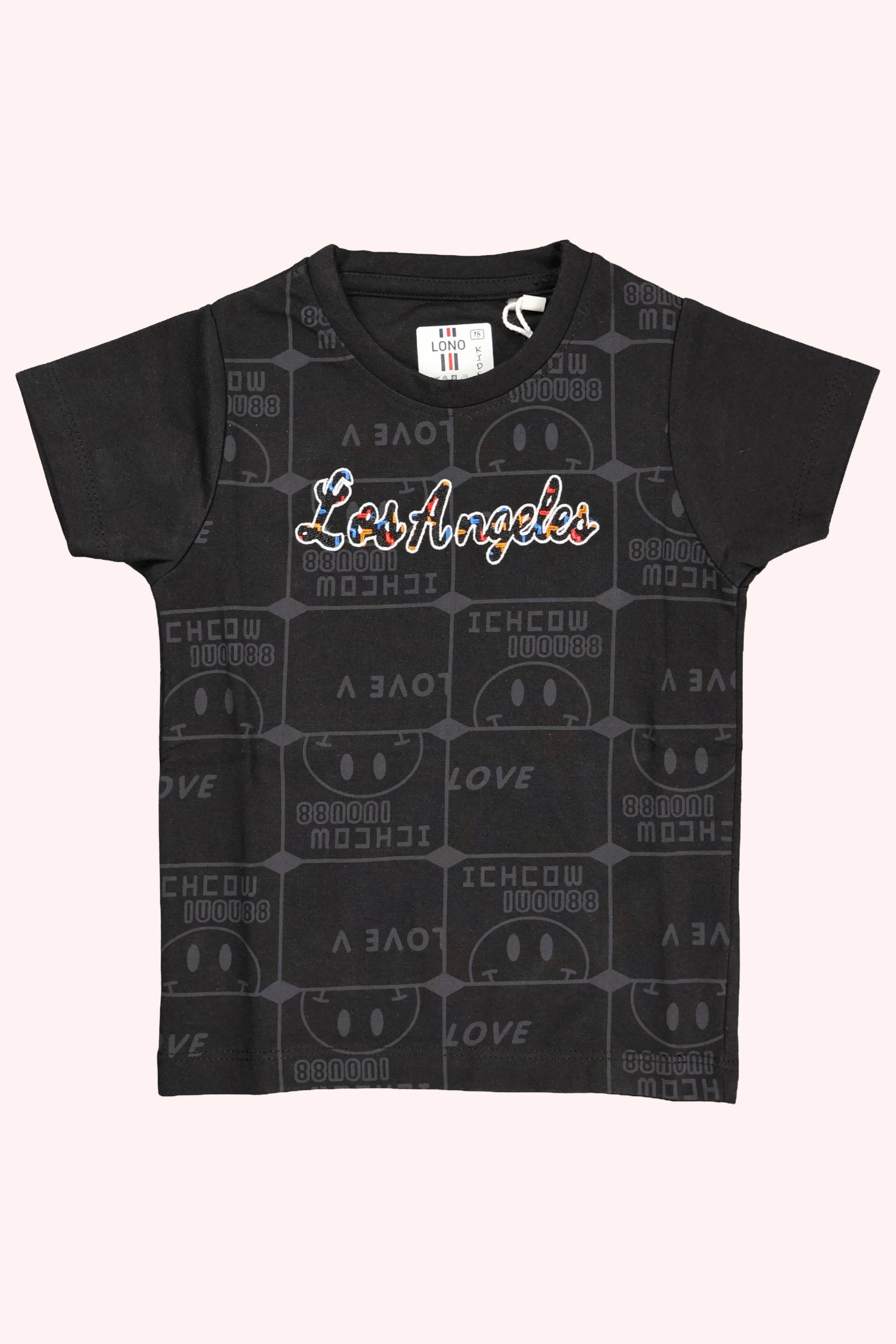 A children's black short-sleeve t-shirt. The front features "Los Angeles" written in a colorful script font over a subtle, all-over dark grey repeating "Love" typography pattern. The shirt is displayed as a flat lay against a light pink and white background.