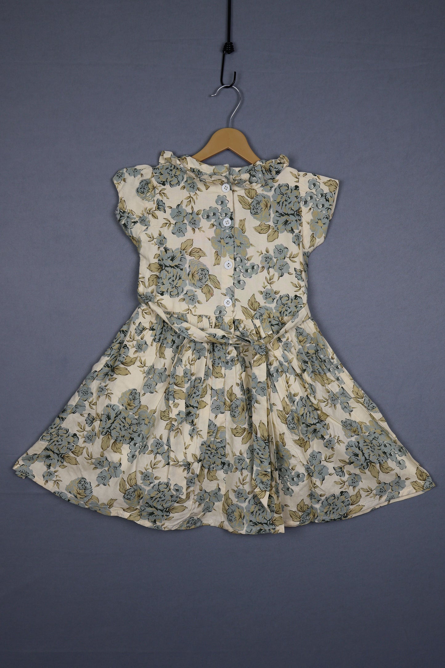 Floral cotton kids dress with buttons, short sleeves, and pastel prints on a hanger