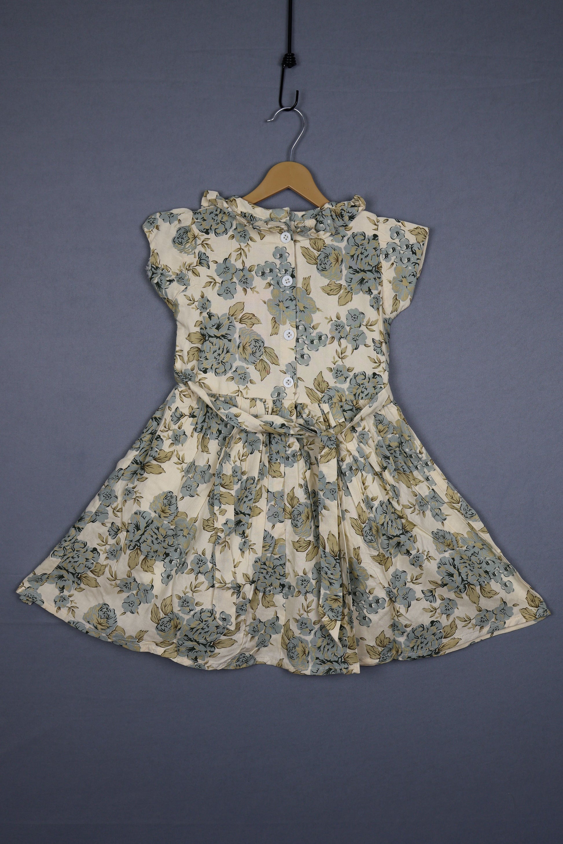 Floral cotton kids dress with buttons, short sleeves, and pastel prints on a hanger