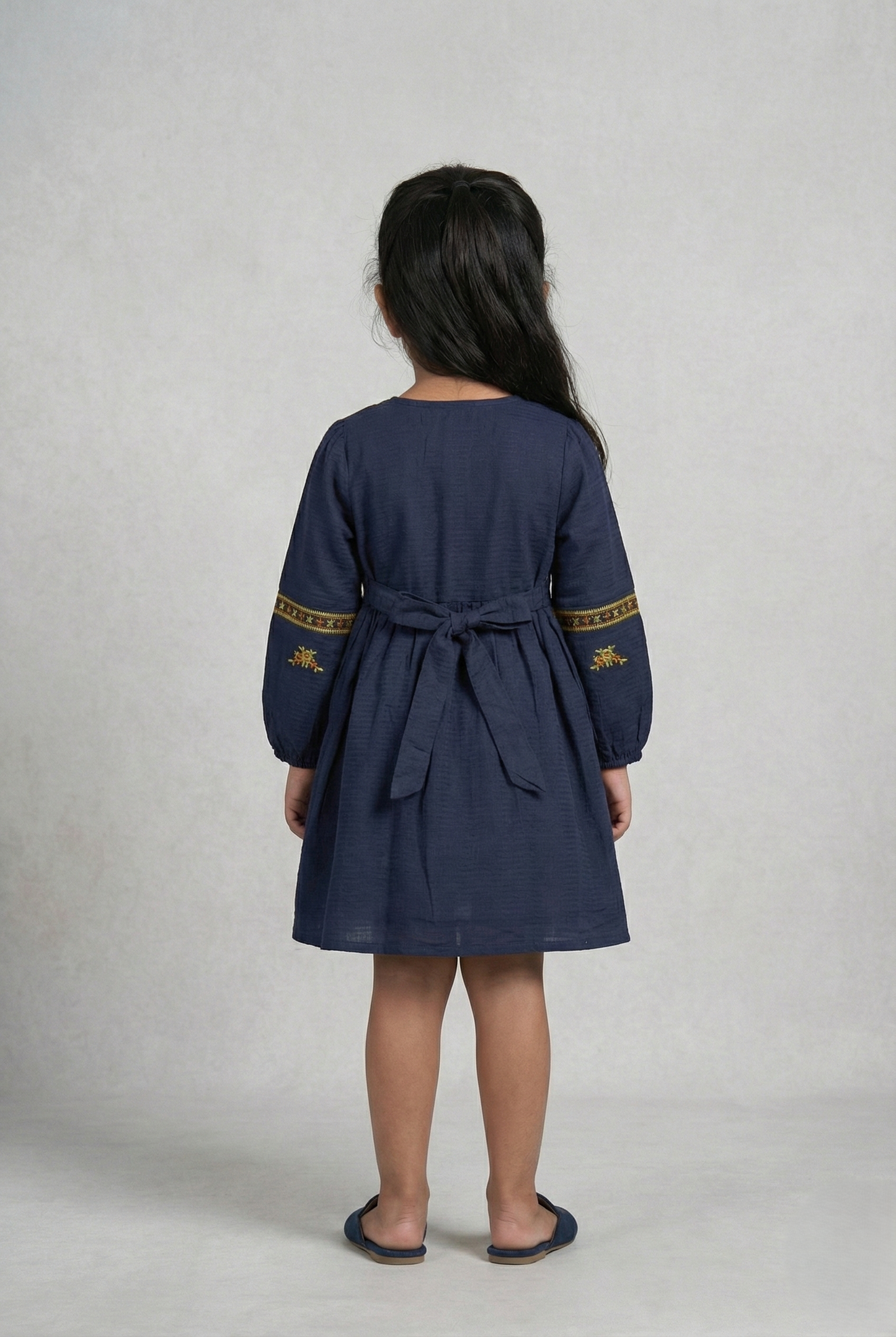 Girl wearing navy blue embroidered cotton frock with long sleeves, viewed from back