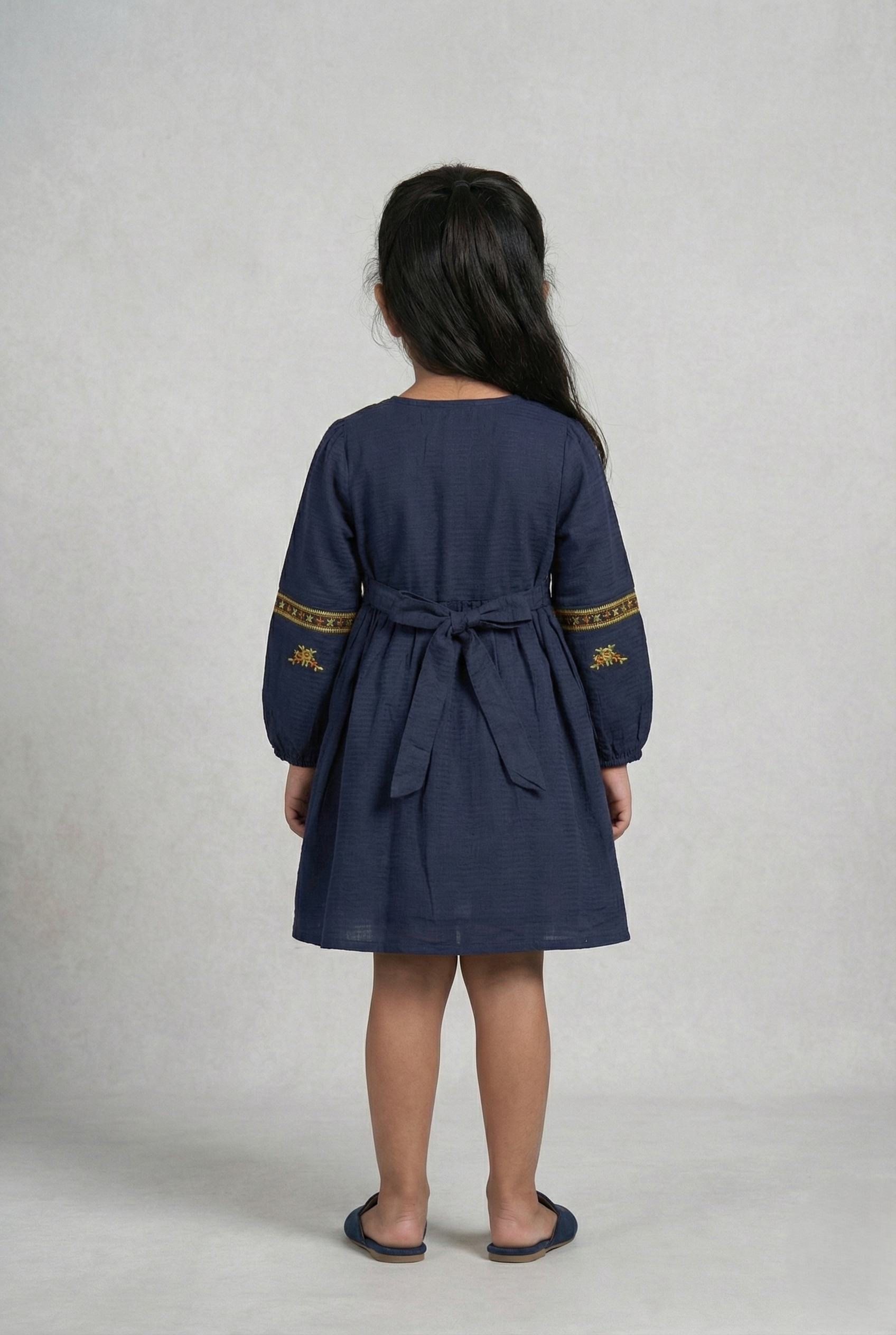 Girl wearing navy blue embroidered cotton frock with long sleeves, viewed from back