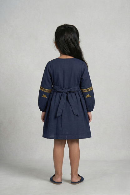 Girl wearing navy blue embroidered cotton frock with long sleeves, viewed from back