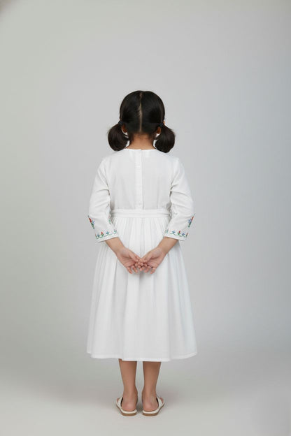 Girl in ivory white embroidered cotton frock standing with hands behind back