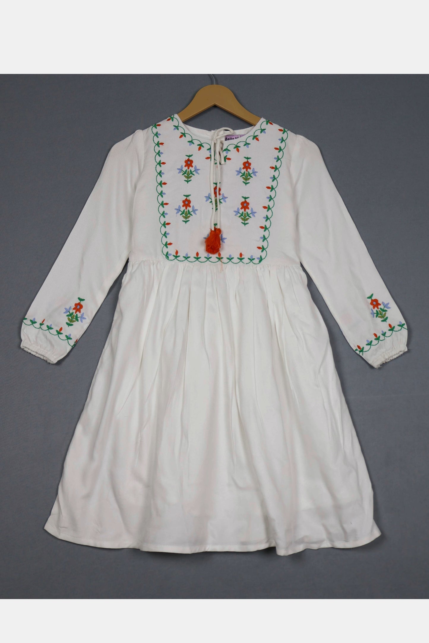 Ivory white cotton frock for girls with colorful floral embroidery, long sleeves, hanging on a hanger.