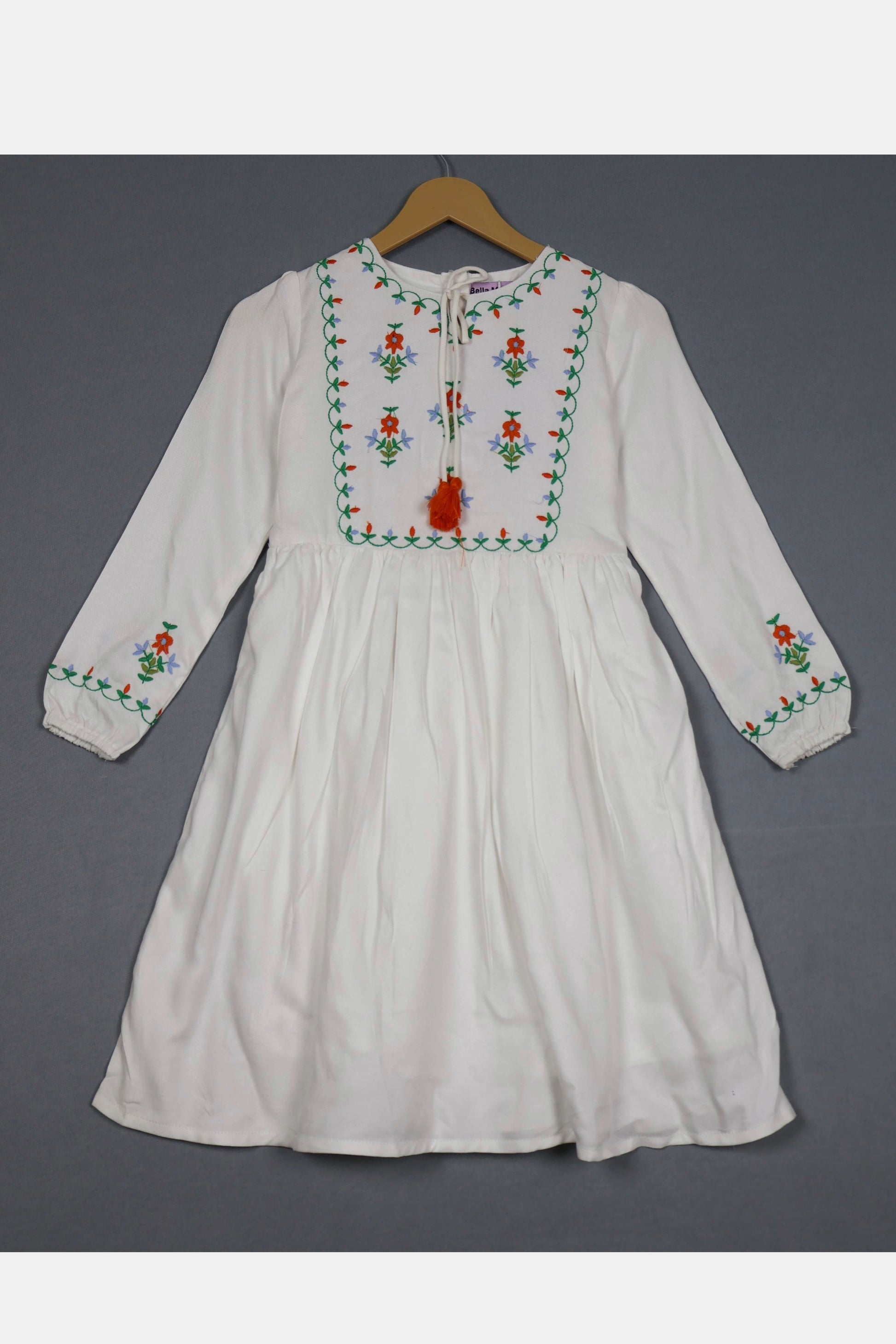 Ivory white cotton frock for girls with colorful floral embroidery, long sleeves, hanging on a hanger.
