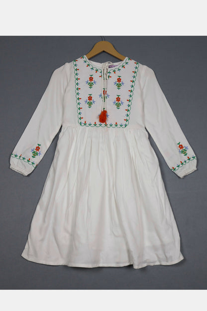 Ivory white cotton frock for girls with colorful floral embroidery, long sleeves, hanging on a hanger.