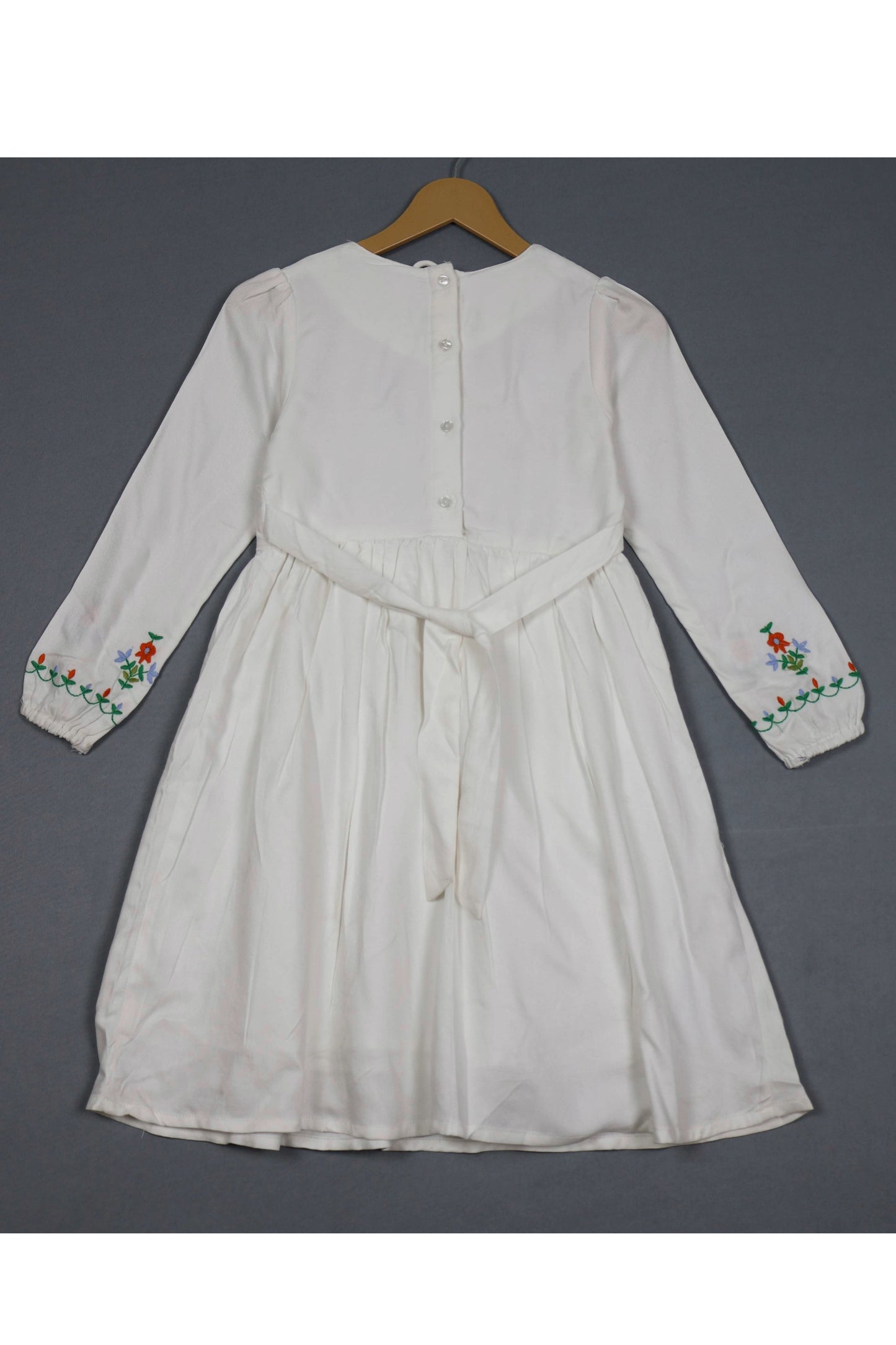 White dress with floral embroidery on a hanger against a gray background