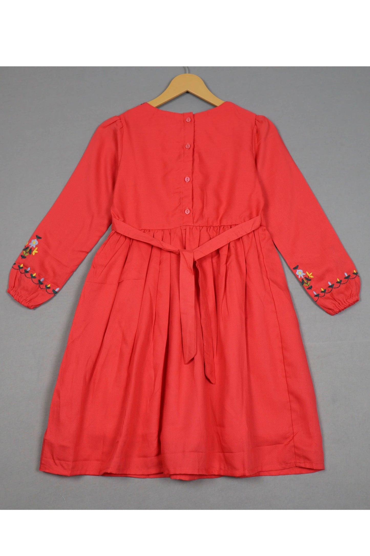 Crimson red cotton girls frock with floral embroidery on sleeves, back buttons, and waist tie.