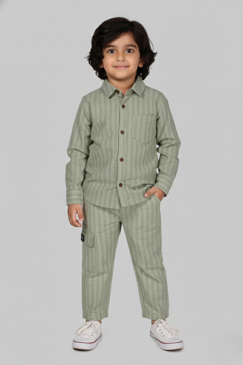 "A detailed product showcase featuring the Fyst boys' pistachio green striped co-ord set. The primary image shows a young boy modeling the complete set, which includes a long-sleeved button-down shirt with fine vertical pinstripes and matching straight-cut trousers. The shirt features a classic spread collar, a single chest pocket, and prominent dark red contrast buttons. The accompanying thumbnails highlight the individual pieces, specifically showing the trousers with a comfortable elasticated waistband a