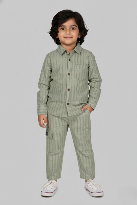 "A detailed product showcase featuring the Fyst boys' pistachio green striped co-ord set. The primary image shows a young boy modeling the complete set, which includes a long-sleeved button-down shirt with fine vertical pinstripes and matching straight-cut trousers. The shirt features a classic spread collar, a single chest pocket, and prominent dark red contrast buttons. The accompanying thumbnails highlight the individual pieces, specifically showing the trousers with a comfortable elasticated waistband a
