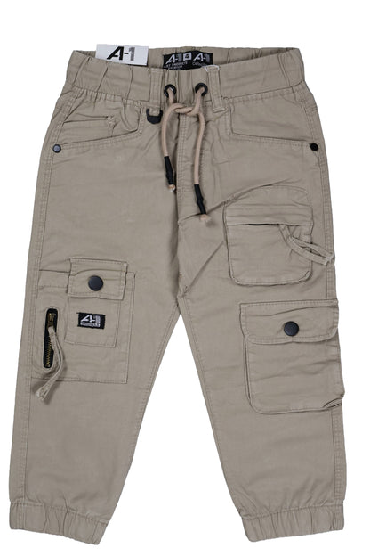 A single piece of children's utility cargo joggers in a light khaki or stone color. The design features a multi-pocket layout including large side flap pockets with black buttons and a vertical zipper detail on the right leg. It has a comfortable elastic waistband with a striped drawstring and elasticated ankle cuffs, shown as a flat lay against a neutral background.